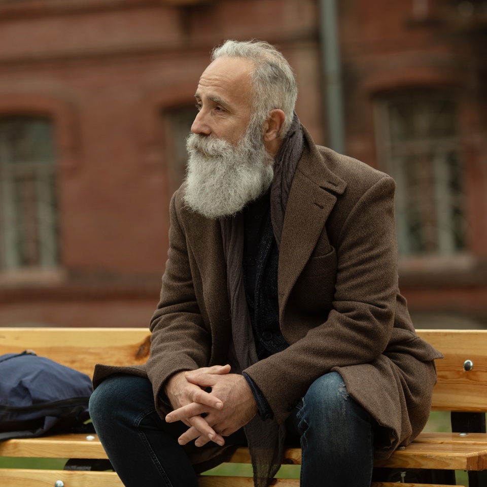 Portrait of a bearded senior man outdoors, sitting on a bench in a park