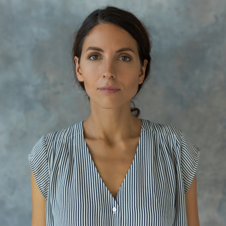 Horizontal indoor portrait of charming young lady posing for ID or passport photo, having calm face expression, looking straight at camera without smile, standing against textured studio wall