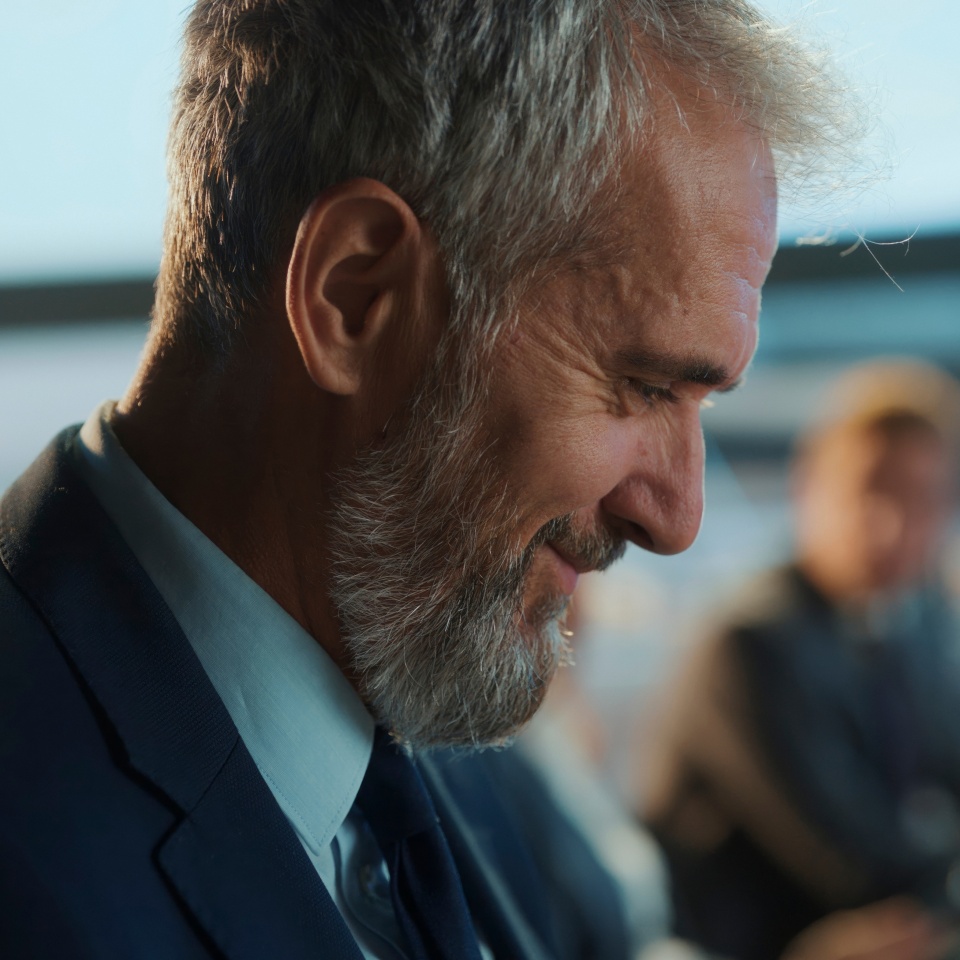 Bearded mature executive smiling contentedly while waiting for his flight in the airport lounge, exuding confidence and relaxation