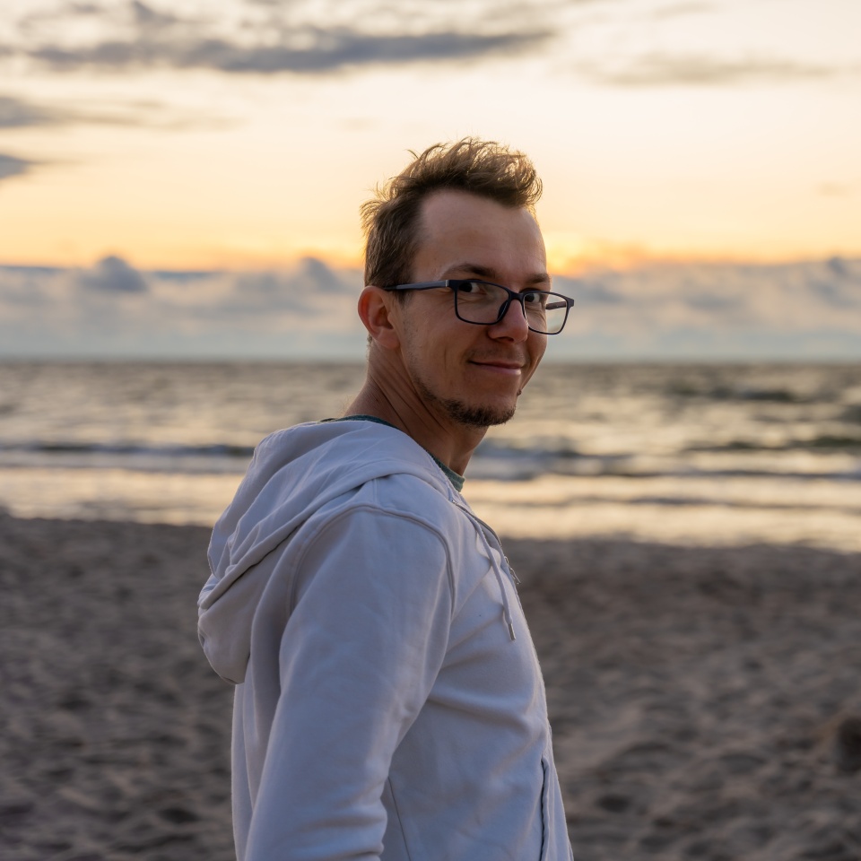 Man in hoodie walking on beach at sunset with smile, relaxed mood and serene sea in background, travel and lifestyle