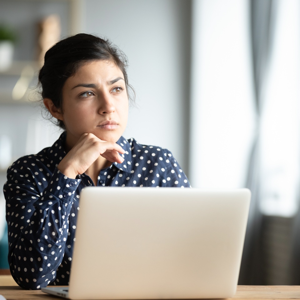 Serious thoughtful pensive young indian ethnic woman student sit at home office desk with laptop thinking of inspiration solution lost in thoughts dreaming looking away search creative ideas concept