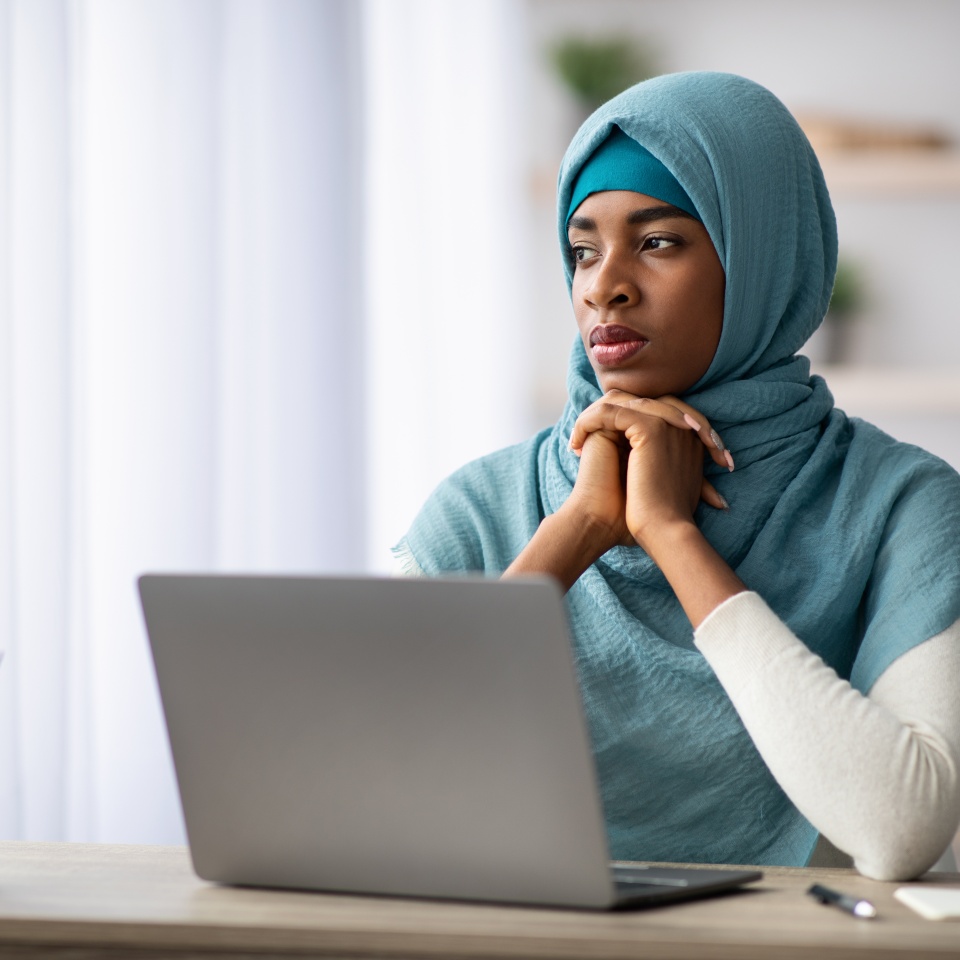Portrait Of Pensive Black Islamic Lady In Hijab Sitting At Desk With Laptop, Thoughtful Muslim Woman Thinking About Something While Working With Computer In Home Office, Having Inspiration Crisis