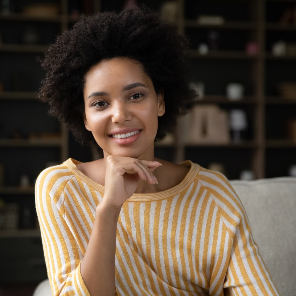 Happy millennial African American girl home head shot portrait. Smiling young woman looking at camera, talking on video call, sitting on couch, speaking online, touching face. Screen view