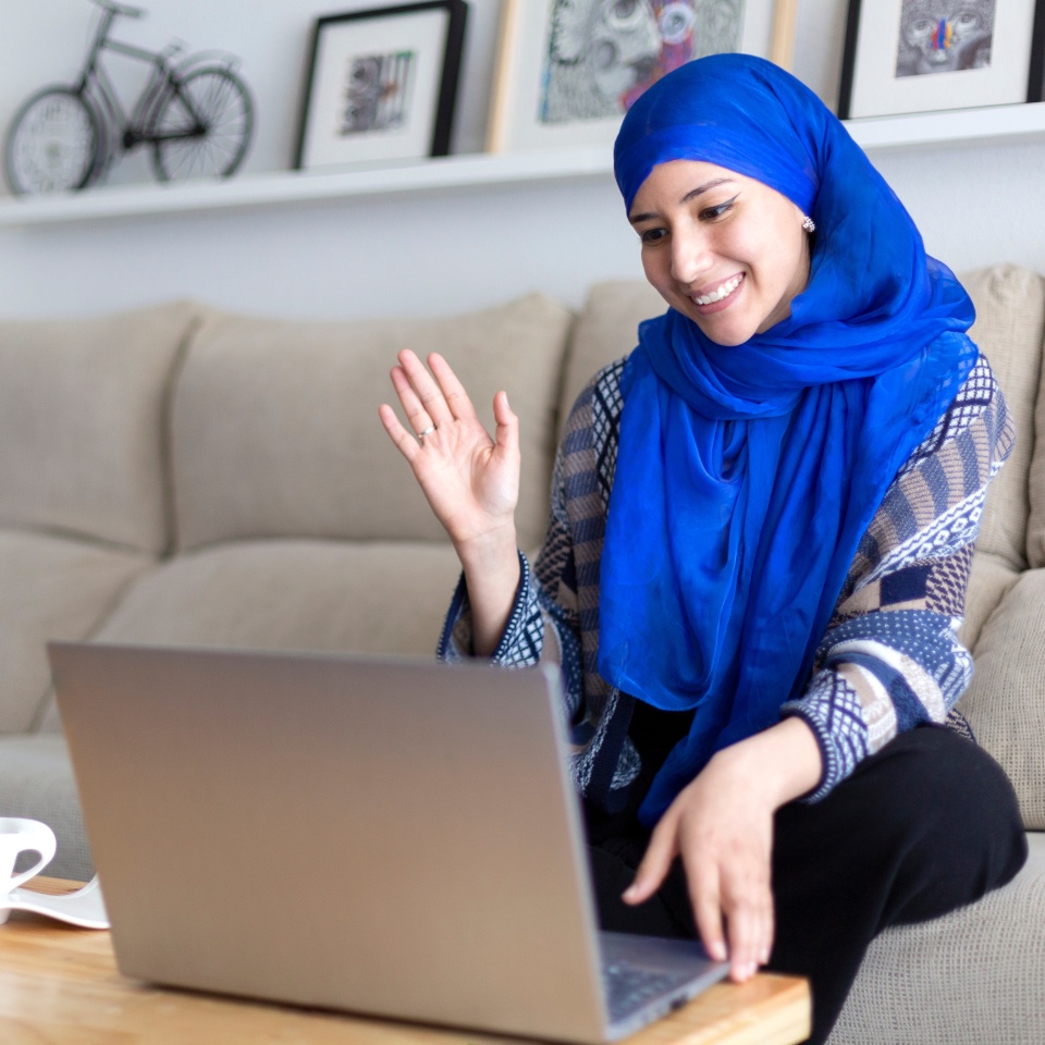 Smiling young Muslim woman making a video conference through laptop. Remote relationships. Space for text.