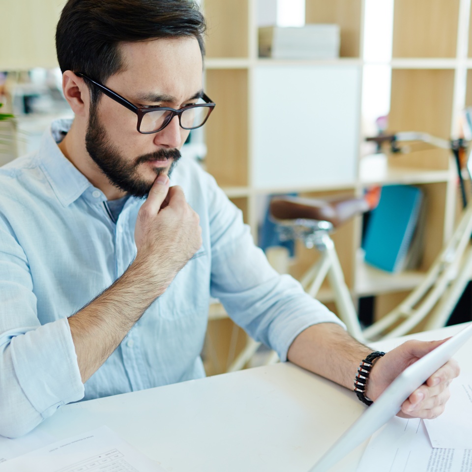 Portrait of contemporary Asian man working in office using digital tablet and thinking about project